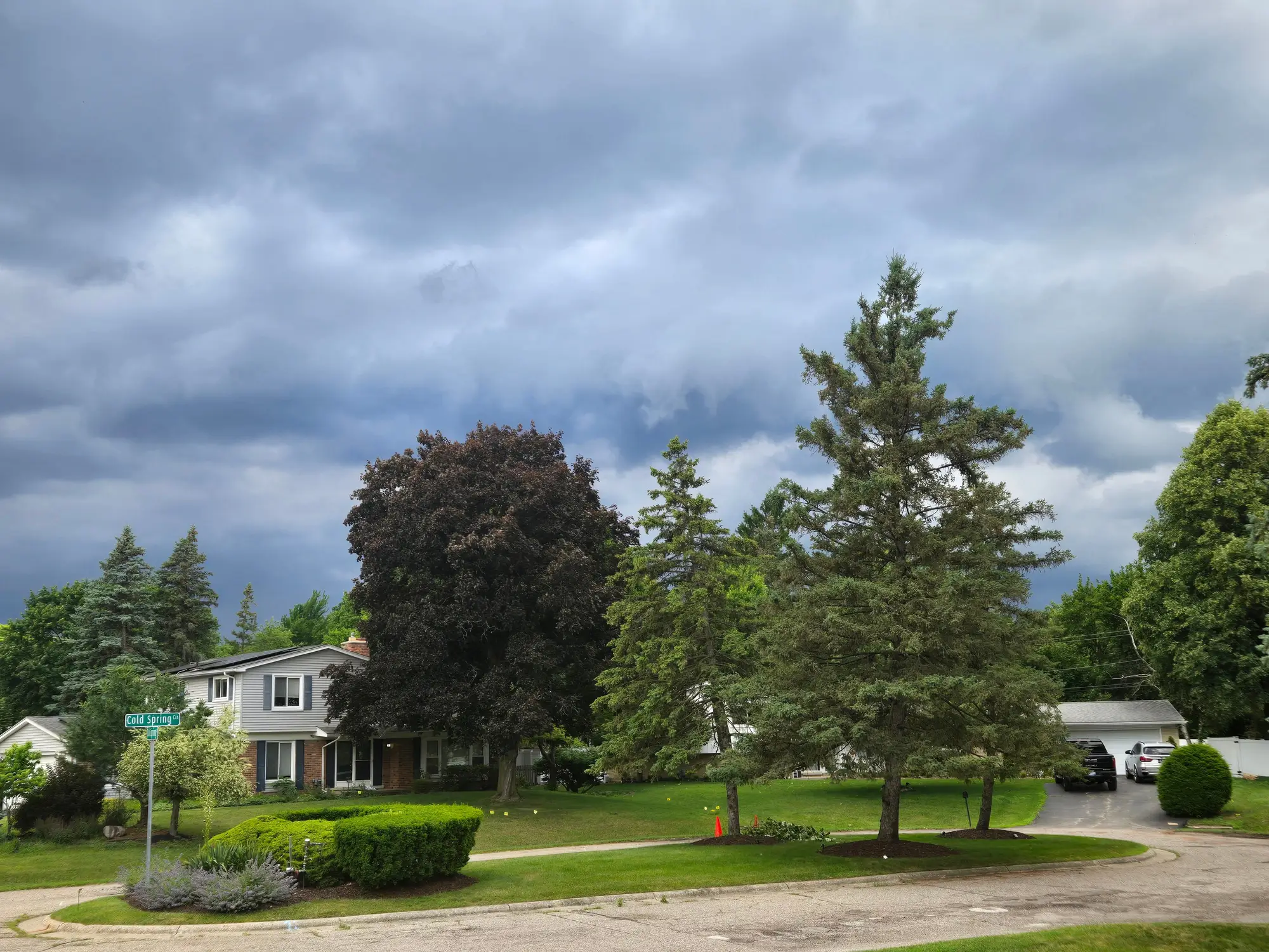 Grey storm clouds building over a suburban street of houses and tall pines